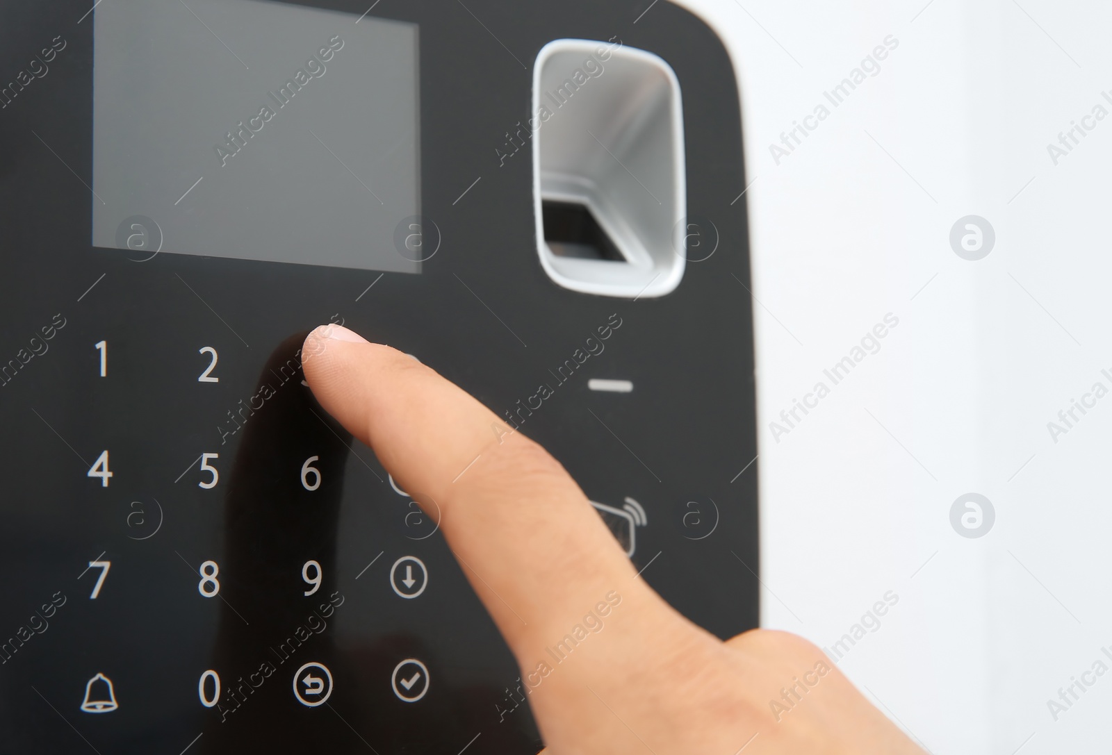 Photo of Young man entering code on alarm system keypad indoors