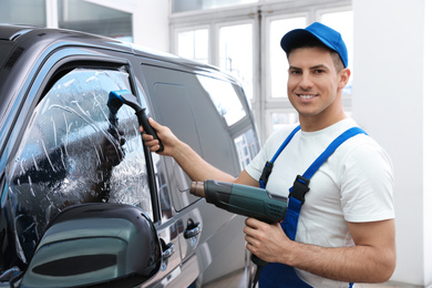 Photo of Worker tinting car window with foil in workshop