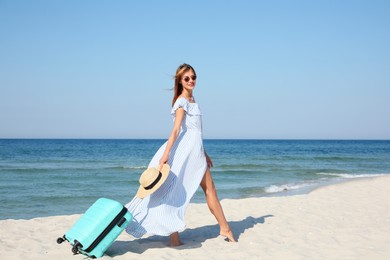 Photo of Beautiful woman with suitcase on sandy beach near sea