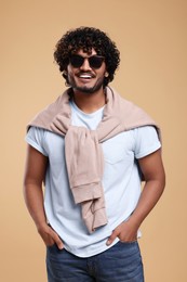 Photo of Handsome young smiling man in sunglasses on beige background