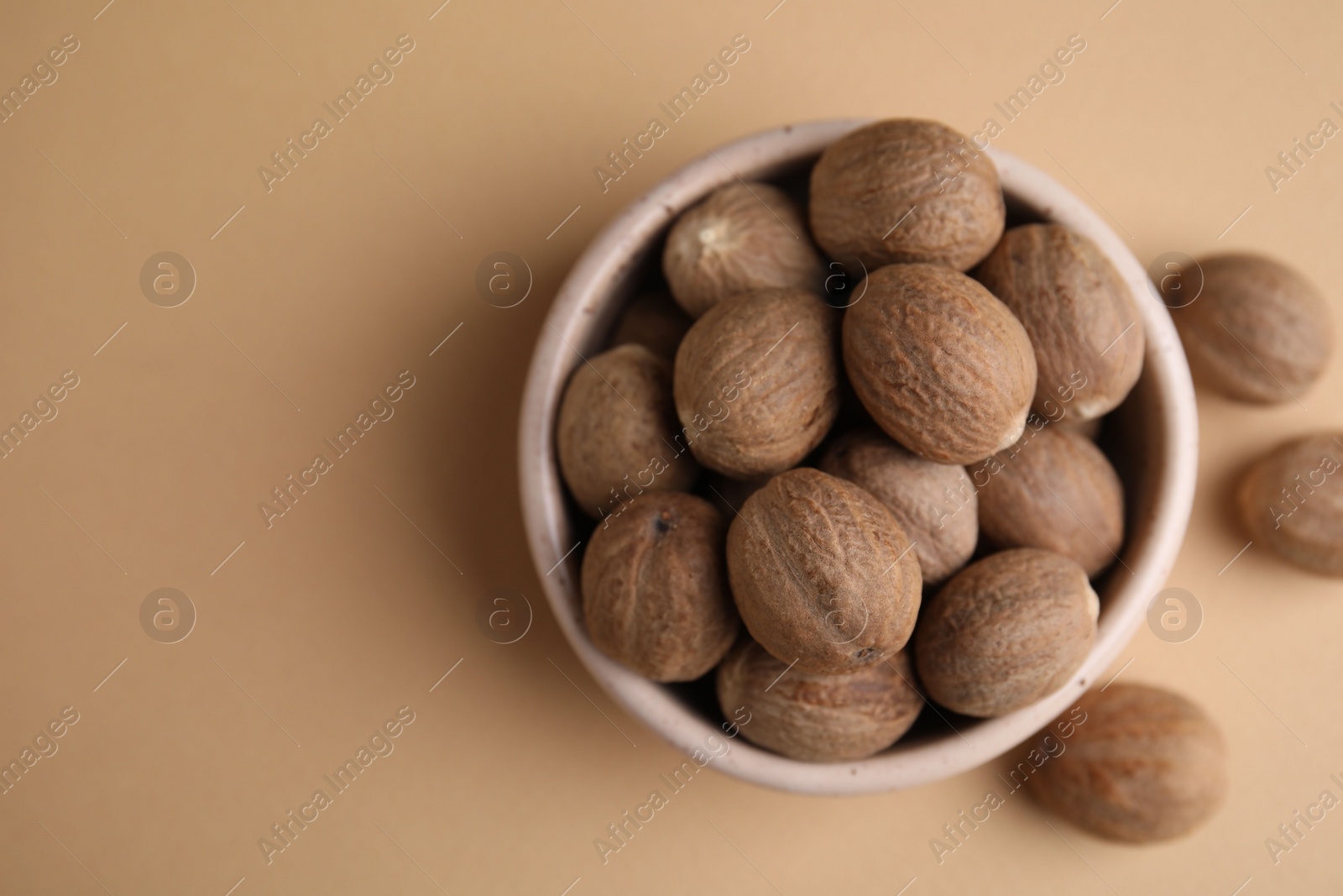 Photo of Whole nutmegs in bowl on light brown background, top view. Space for text