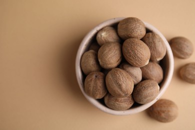 Whole nutmegs in bowl on light brown background, top view. Space for text