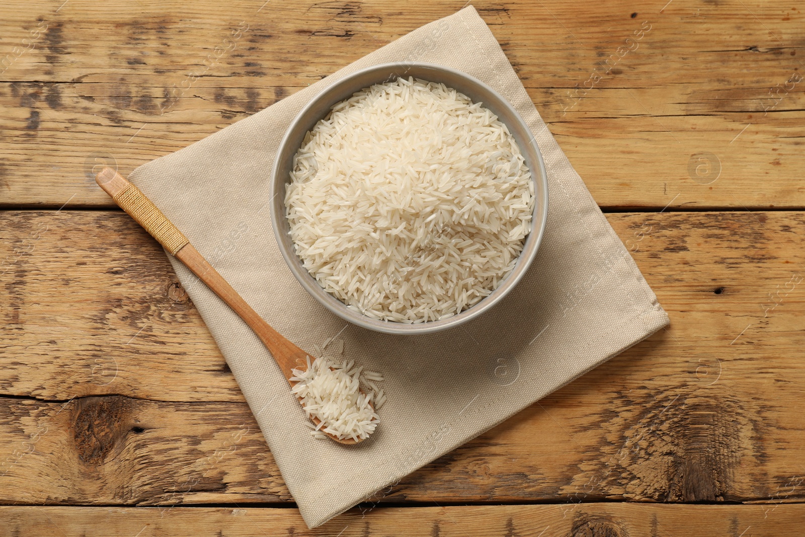 Photo of Raw basmati rice in bowl and spoon on wooden table, top view