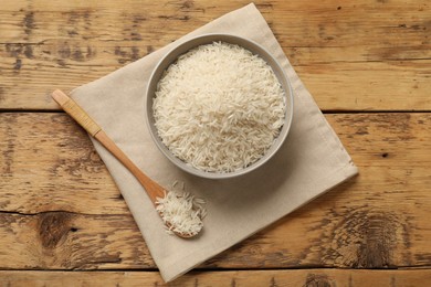 Photo of Raw basmati rice in bowl and spoon on wooden table, top view