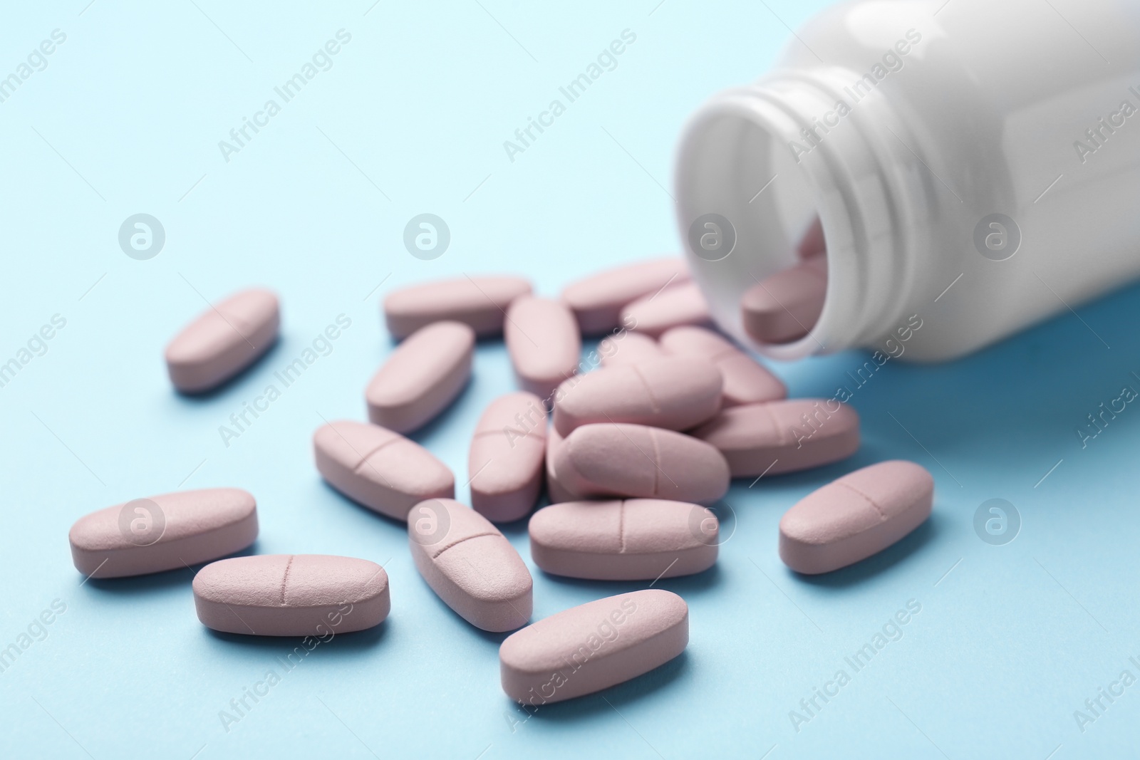 Photo of Vitamin pills and bottle on light blue background, closeup