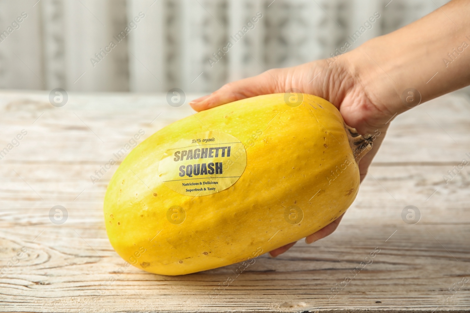 Photo of Woman holding ripe spaghetti squash on wooden table, closeup