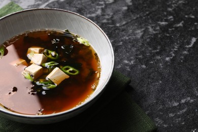 Photo of Bowl of delicious miso soup with tofu on black textured table, space for text