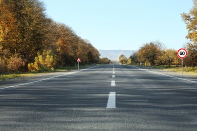 Image of Traffic signs MAXIMUM SPEED 60 and Speed Bump near empty asphalt road in autumn