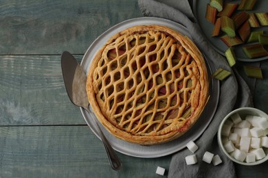 Photo of Freshly baked rhubarb pie, cut stalks, sugar cubes and cake server on wooden table, flat lay