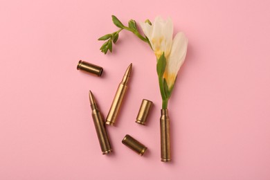 Photo of Bullets and cartridge cases with beautiful flower on pink background, flat lay