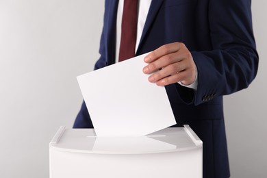 Man putting his vote into ballot box on light grey background, closeup