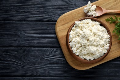 Photo of Delicious fresh cottage cheese with parsley on black wooden table, top view. Space for text