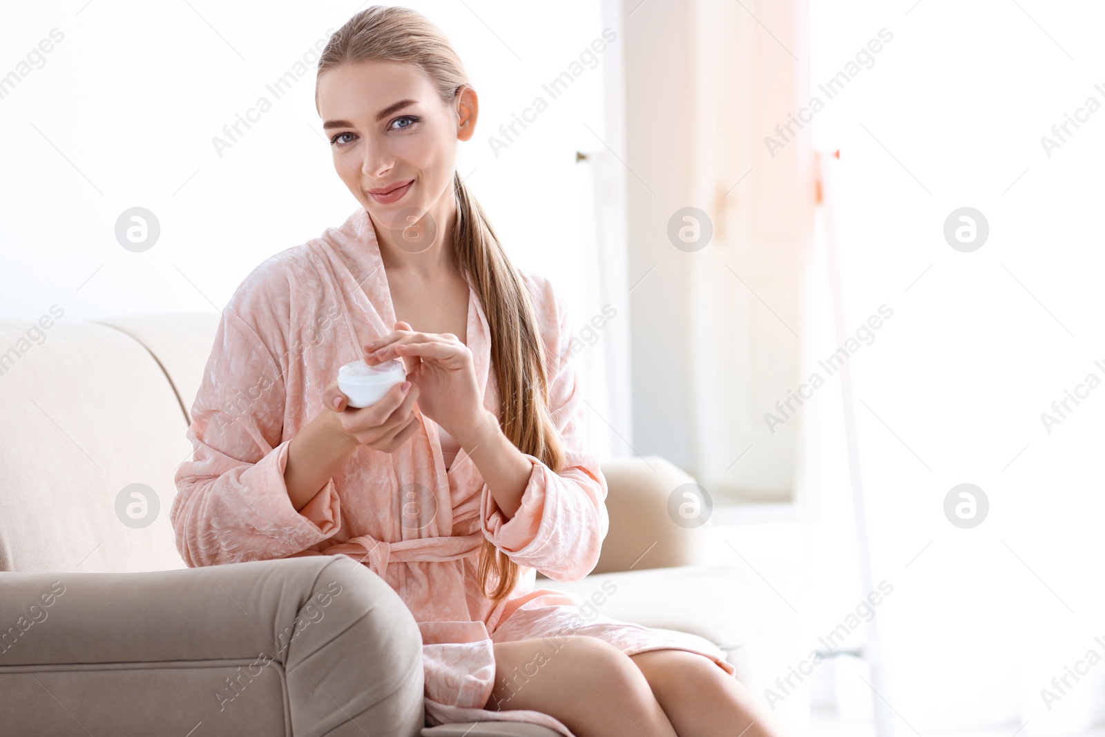 Photo of Young woman with jar of body cream at home