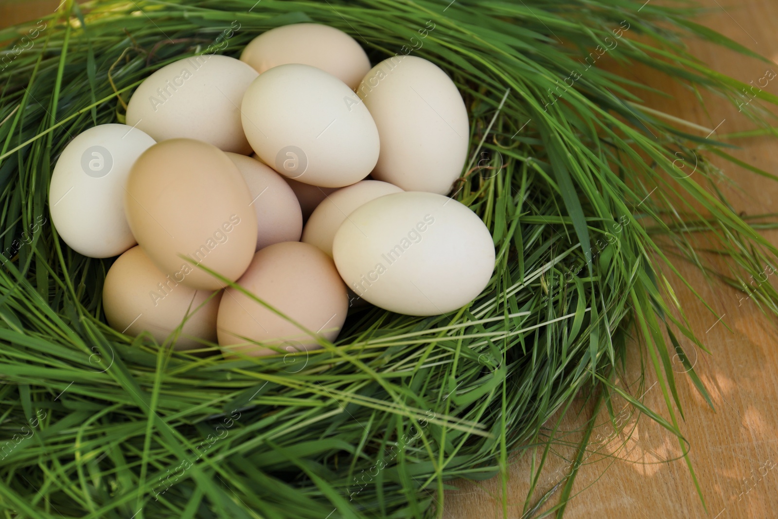 Photo of Nest made of green grass with fresh raw eggs on wooden table, closeup