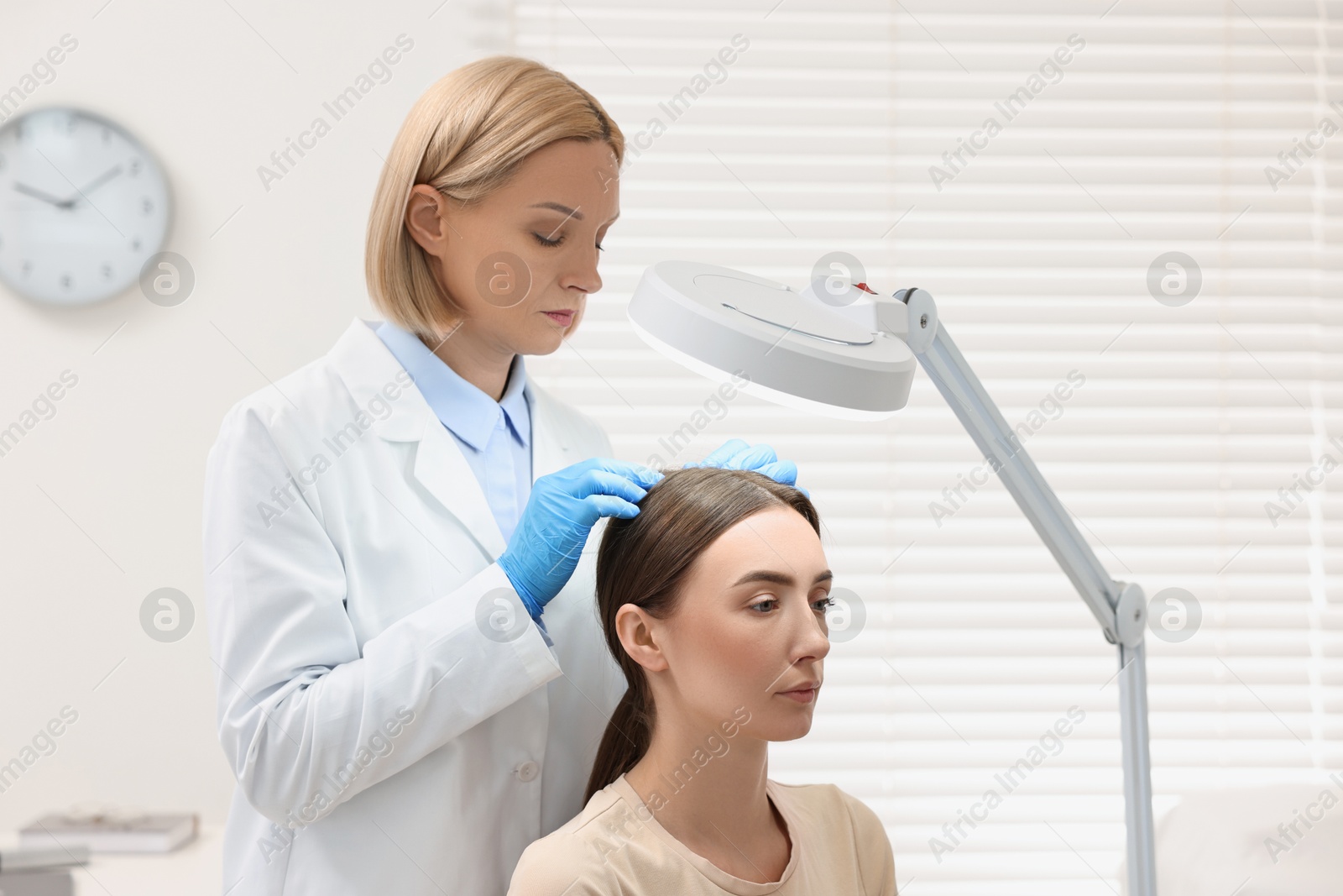 Photo of Trichologist examining patient`s hair under lamp in clinic