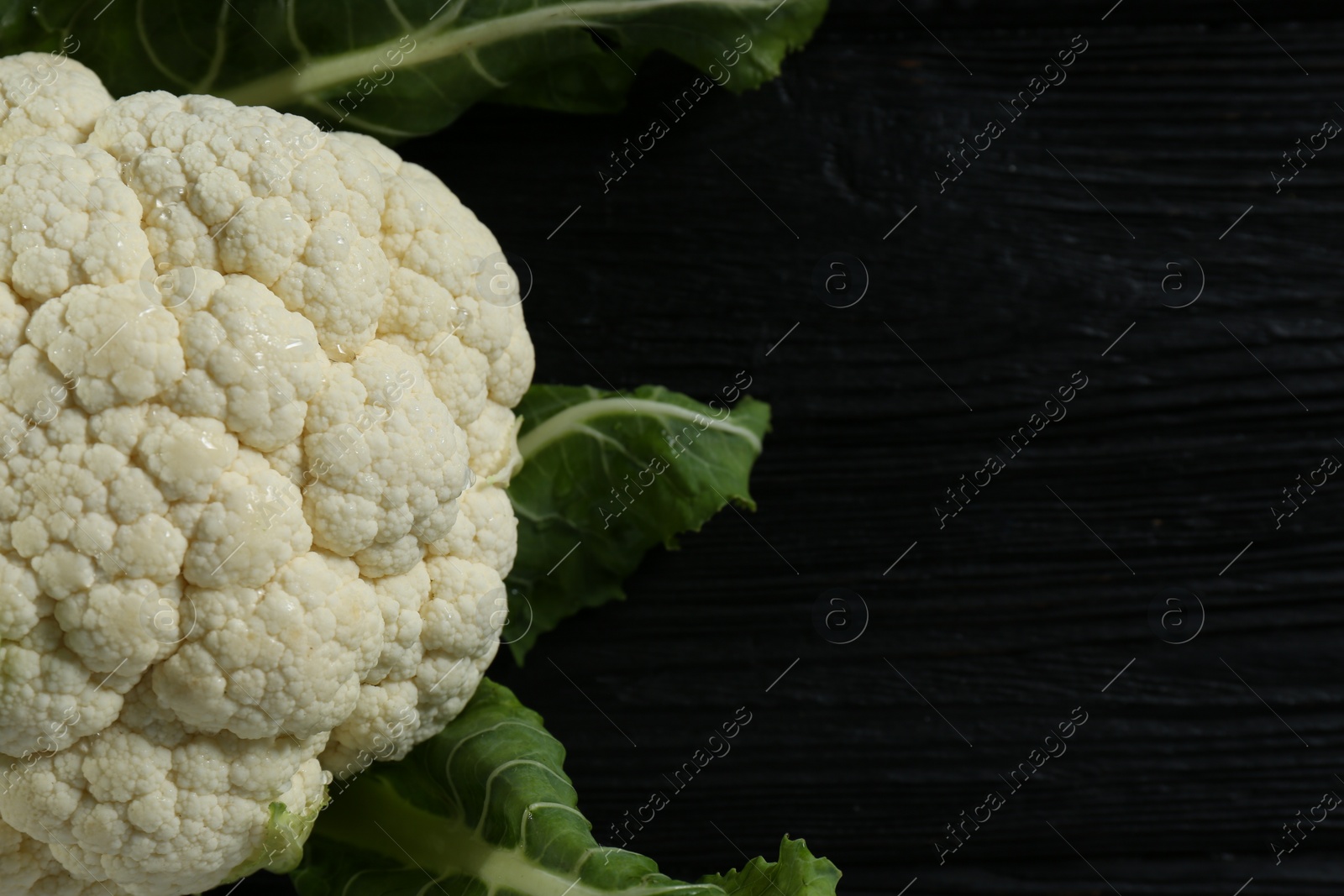 Photo of Fresh whole cauliflower on black wooden table, top view. Space for text