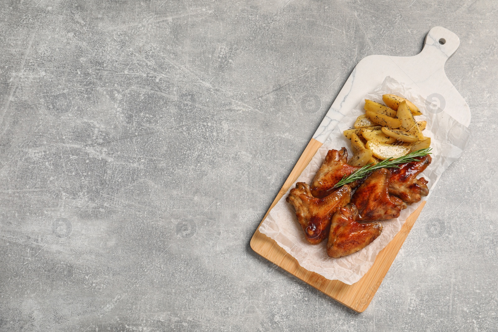 Photo of Delicious fried chicken wings served with baked potatoes on table, top view. Space for text