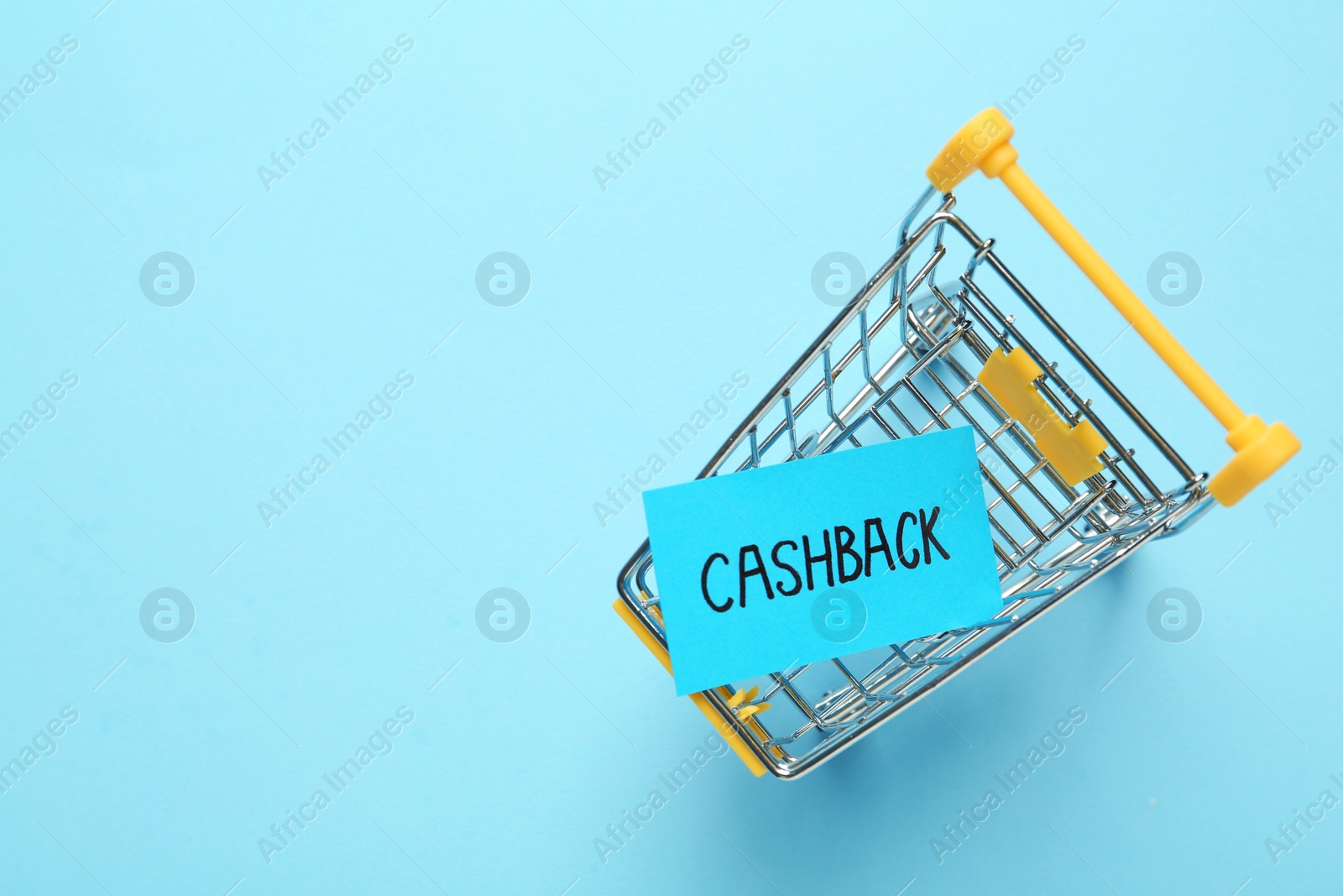 Photo of Card with word Cashback in shopping cart on light blue background, top view. Space for text