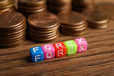 Photo of Word Forex made of colorful cubes with letters and stacked coins on wooden table, closeup