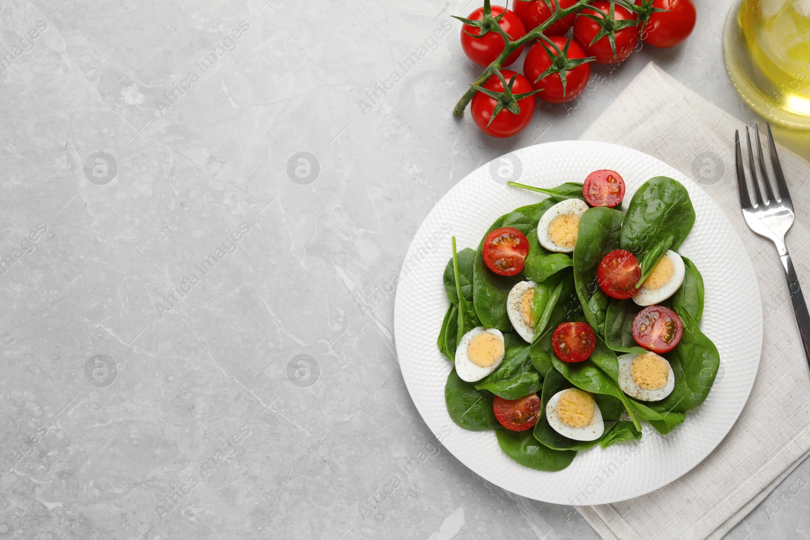Photo of Delicious salad with boiled eggs, tomatoes and spinach served on light grey table, flat lay. Space for text