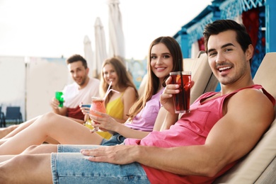 Photo of Happy young friends with fresh summer cocktails relaxing on sunbeds