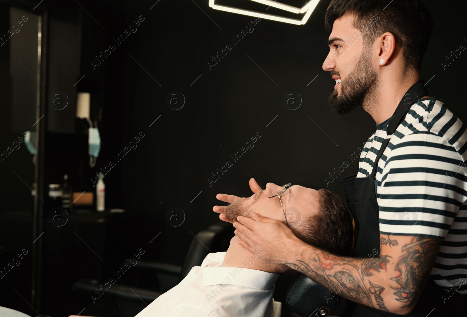 Photo of Hairdresser applying oil onto client's beard in barbershop. Professional shaving service