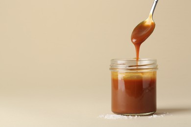 Taking tasty salted caramel with spoon from jar on pale yellow background, space for text