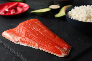 Fresh salmon for sushi and other ingredients on dark table, closeup