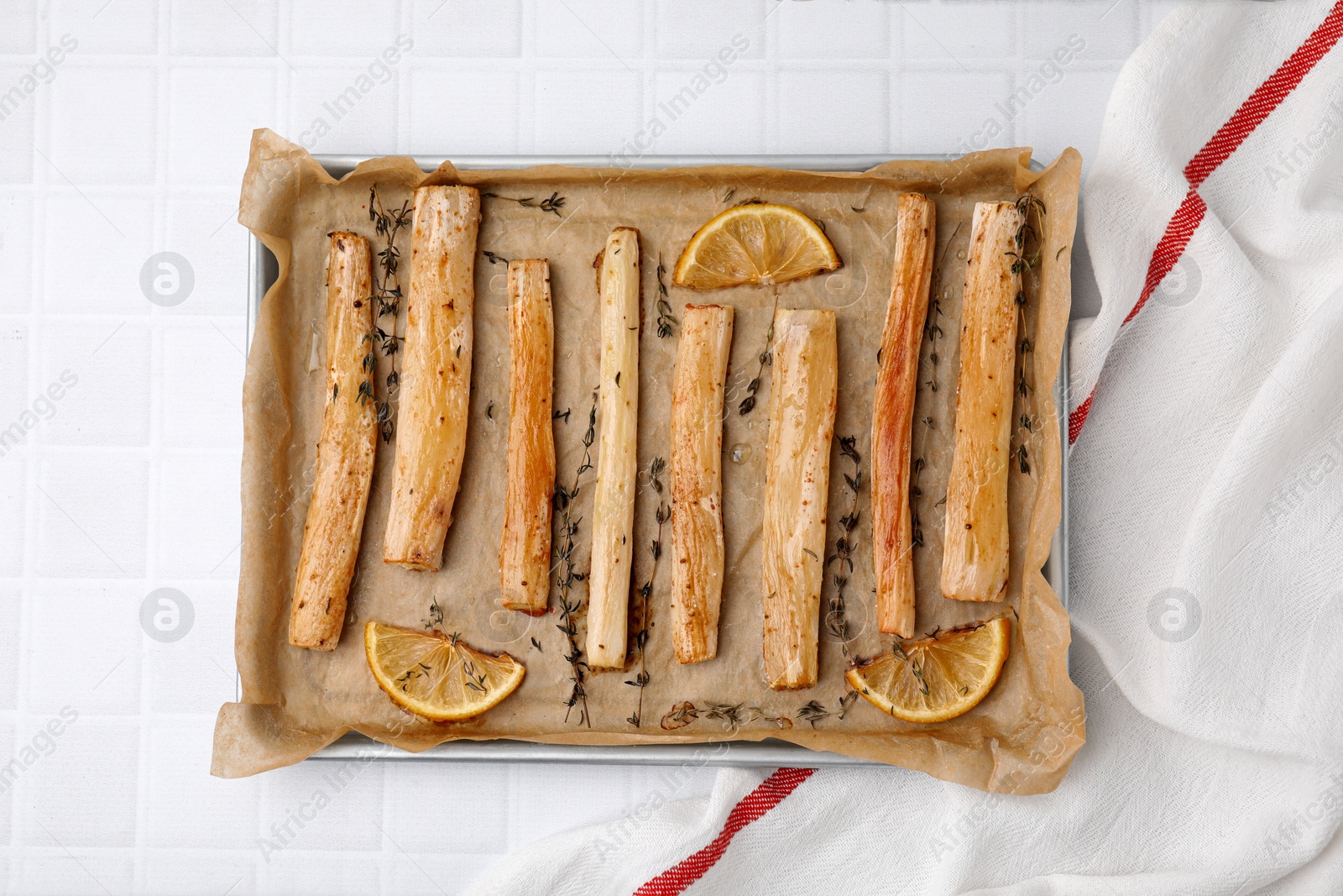 Photo of Baking tray with cooked salsify roots, lemon and thyme on white tiled table, top view