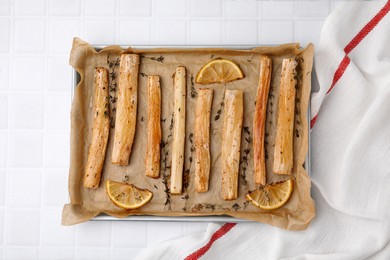 Photo of Baking tray with cooked salsify roots, lemon and thyme on white tiled table, top view