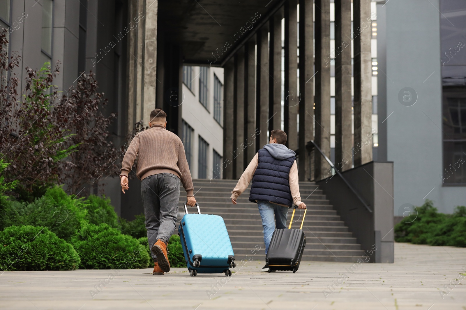 Photo of Being late. Men with suitcases running towards building outdoors, back view
