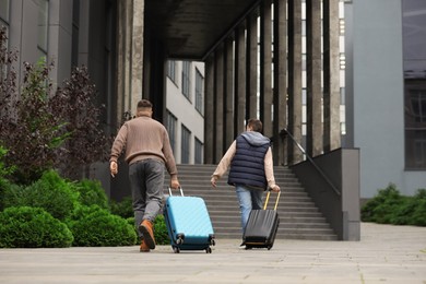 Being late. Men with suitcases running towards building outdoors, back view