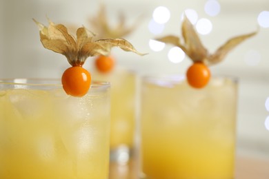 Photo of Refreshing cocktails decorated with physalis fruits against blurred festive lights, closeup