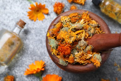 Photo of Wooden mortar with dry calendula flowers on light grey table, flat lay. Space for text