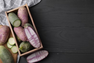 Photo of Purple and green daikon radishes in crate on black wooden table, flat lay. Space for text