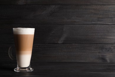 Photo of Glass cup of delicious layered coffee on black wooden table, space for text