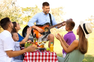 Photo of Man playing guitar for friends at picnic in park