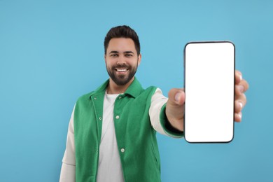 Young man showing smartphone in hand on light blue background