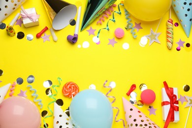 Flat lay composition with party hats and other festive items on yellow background, space for text. Birthday surprise
