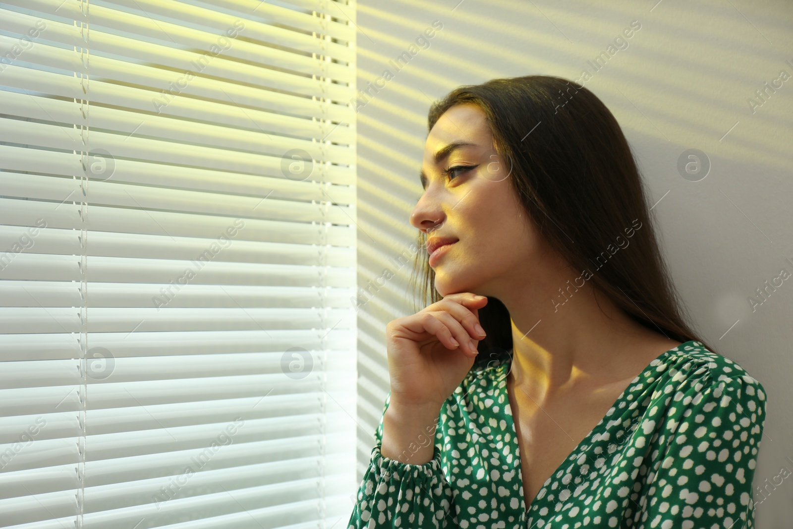 Photo of Young woman near window with Venetian blinds. Space for text