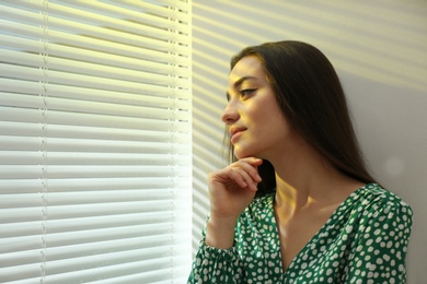 Photo of Young woman near window with Venetian blinds. Space for text