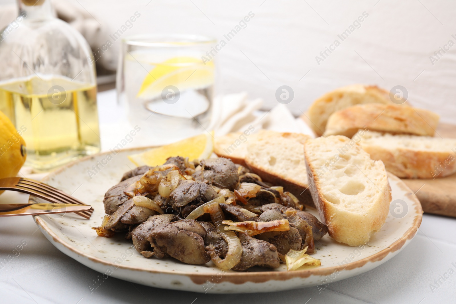 Photo of Tasty fried chicken liver with onion served on white tiled table