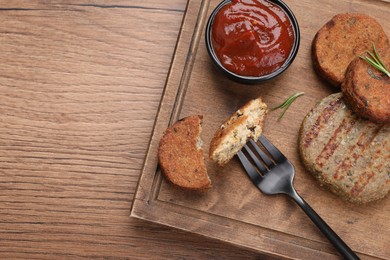 Fork with piece of delicious cutlet near tasty vegan meat products and sauce on wooden table, top view. Space for text