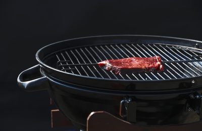 Photo of Tasty steak on modern barbecue grill against dark background
