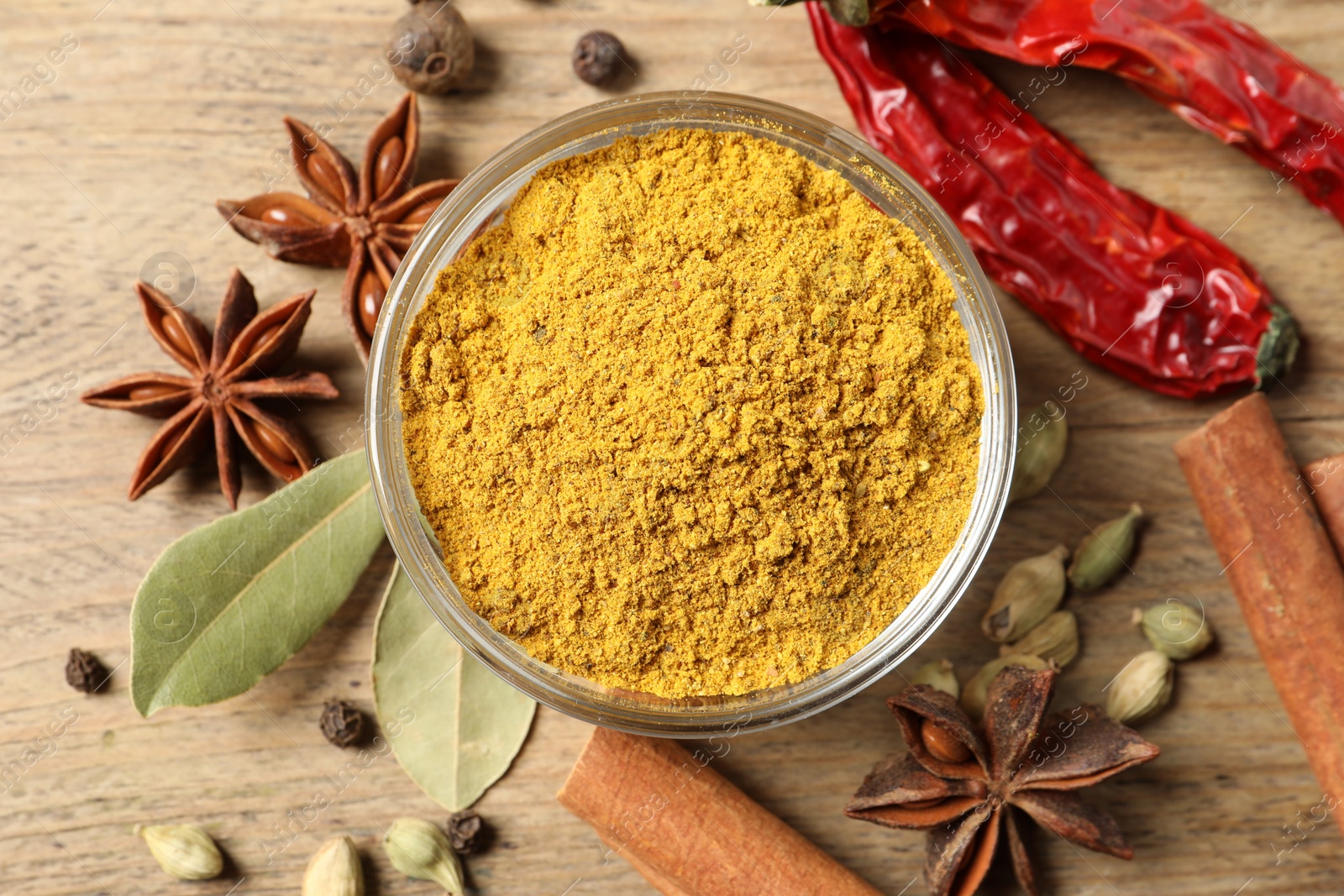 Photo of Curry powder in bowl and other spices on wooden table, flat lay