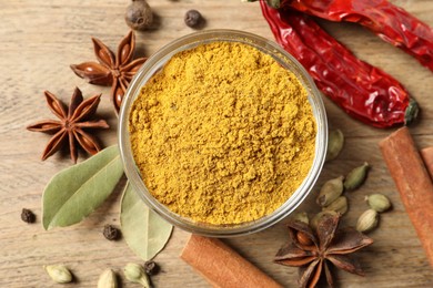 Photo of Curry powder in bowl and other spices on wooden table, flat lay