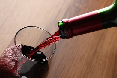 Photo of Pouring tasty red wine in glass at wooden table, closeup