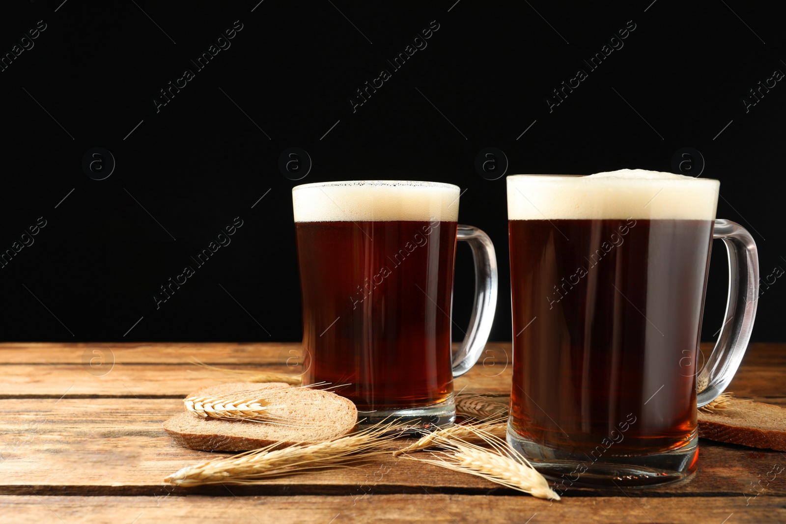 Photo of Mugs of delicious kvass, spikes and bread on wooden table against black background. Space for text