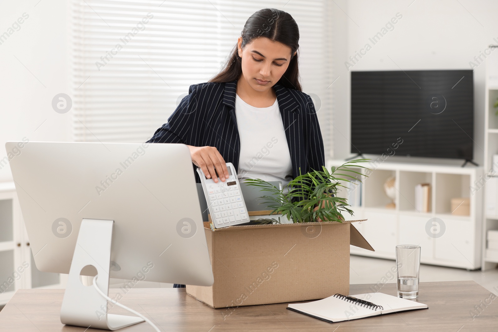 Photo of Unemployment problem. Woman with box of personal belongings at table in office