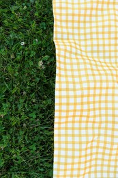 Photo of Checkered picnic tablecloth on fresh green grass, top view. Space for text